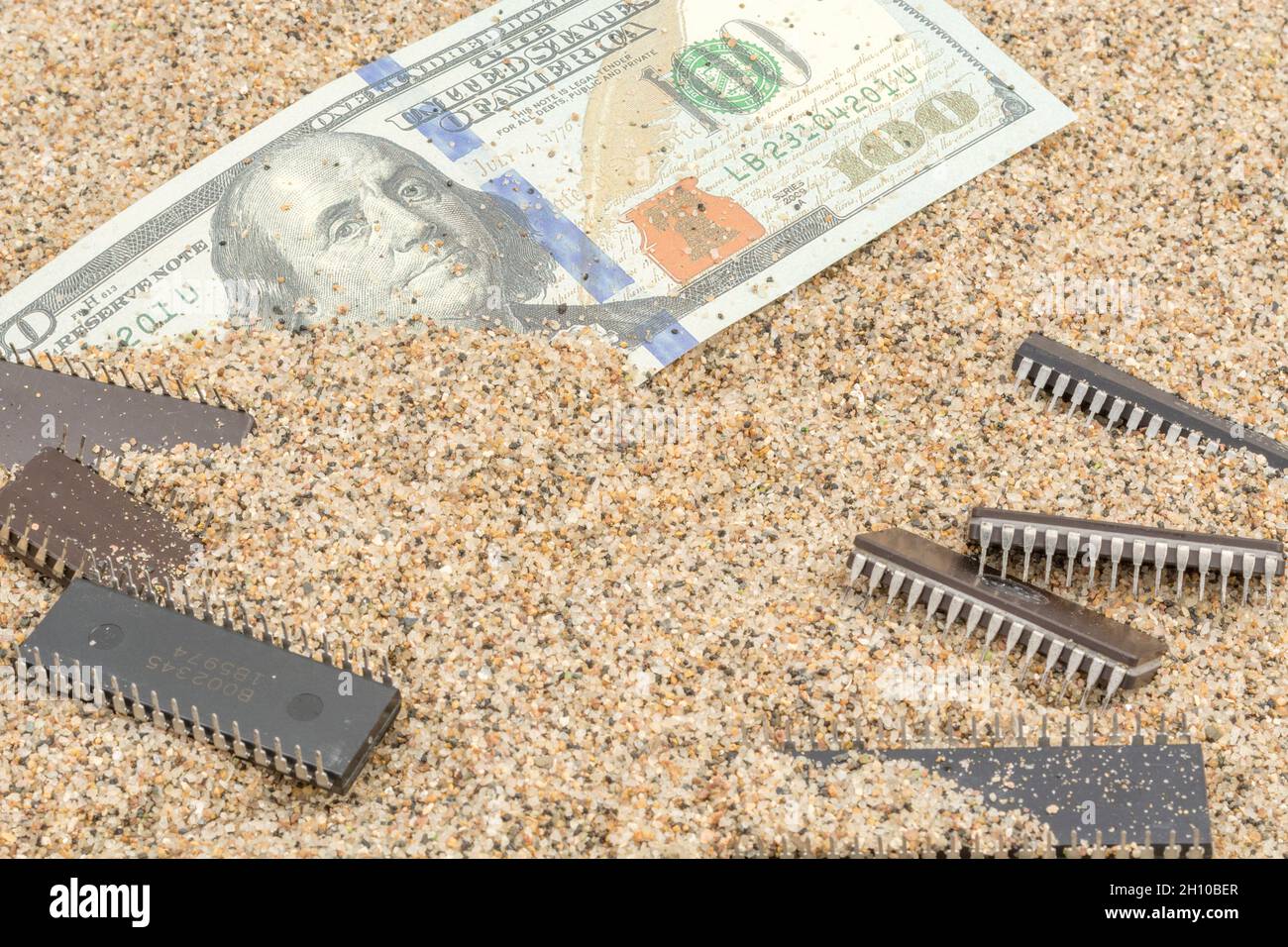 BILLET DE 100 $ US / billet de banque Benjamin Franklin enfoui dans le sable avec une puce.Pour les pénuries de puces de semi-conducteurs aux États-Unis dans le secteur de la technologie. Banque D'Images