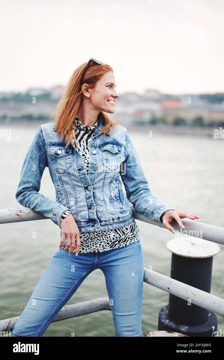 Bonne positive redhead caucasienne femme en denim veste et bleu jeans posant à la berge Banque D'Images