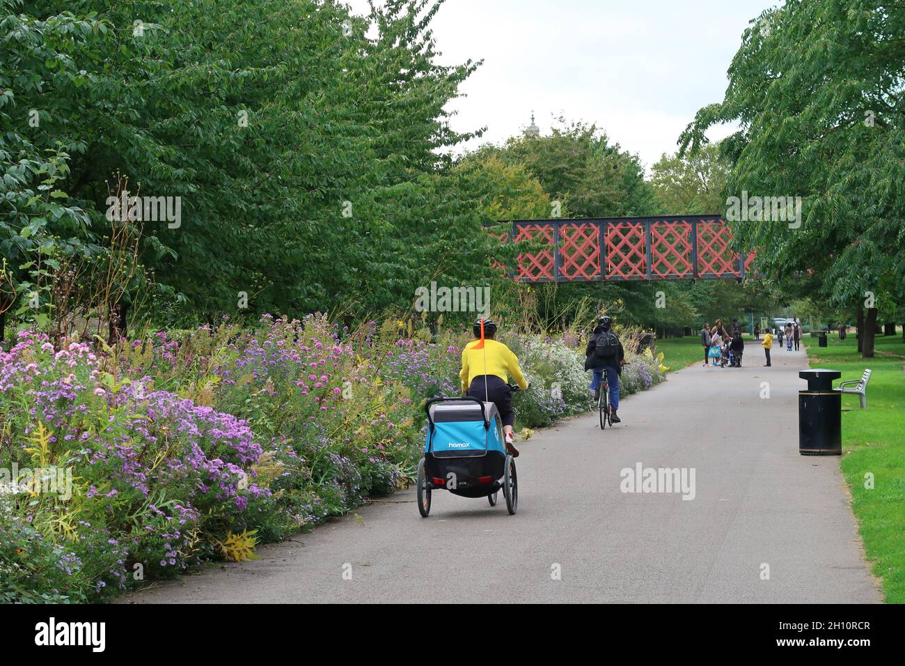 Burgess Park, Peckham, Londres, Royaume-Uni.Un cycliste avec une remorque pour enfants utilise le chemin suivant l'ancien canal de Surrey. Banque D'Images