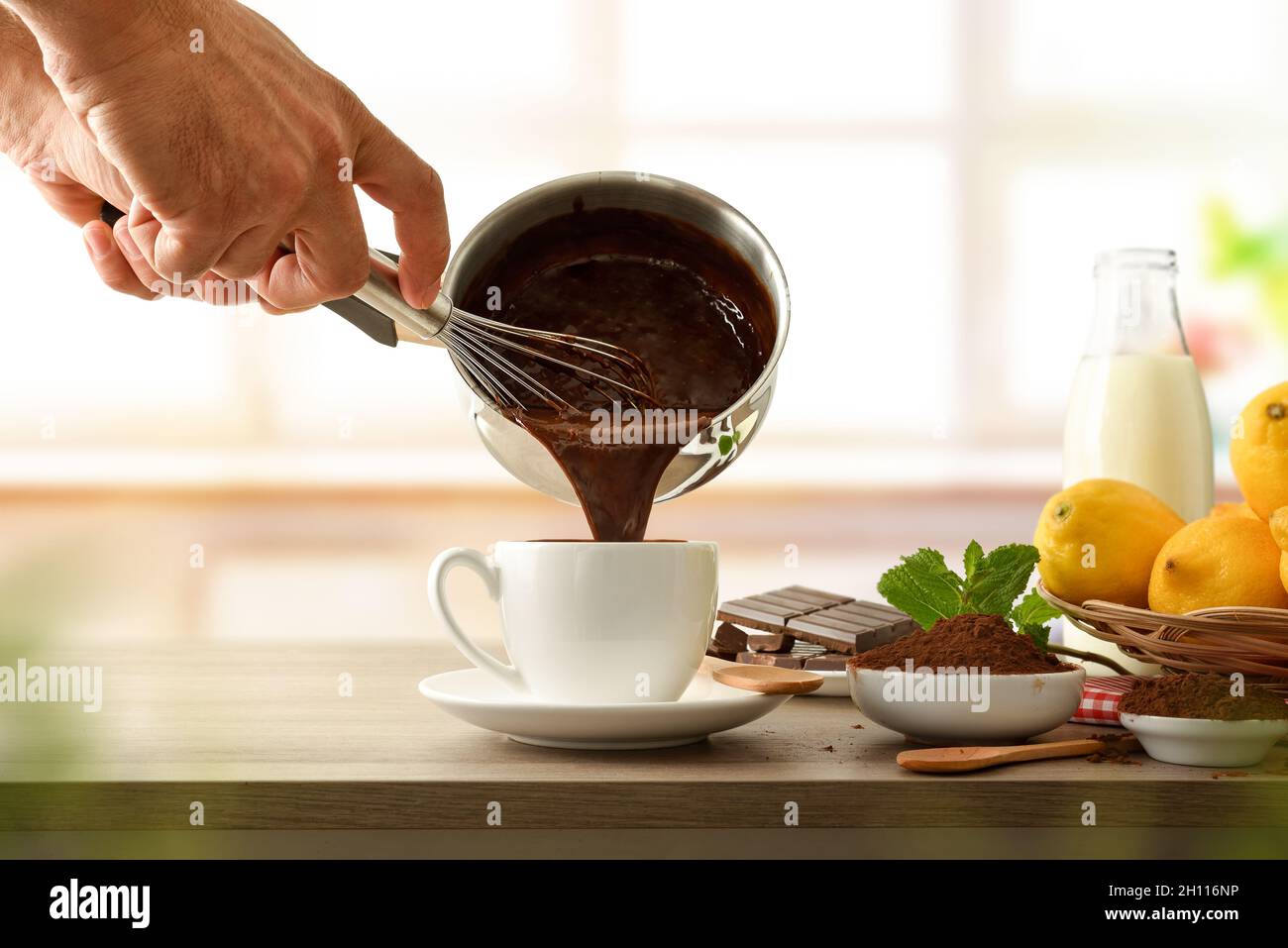Homme remplissant une tasse de chocolat chaud frais maison avec des ingrédients sur le banc de cuisine.Vue avant. Banque D'Images
