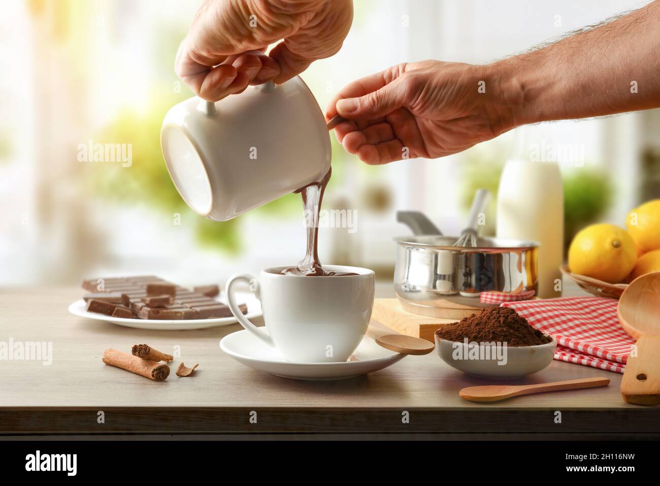 Homme préparant de la crème au chocolat pour un gâteau sur un banc de cuisine avec une barre de chocolat à pâtisserie, de la poudre, de la cannelle et des citrons.Vue avant. Banque D'Images
