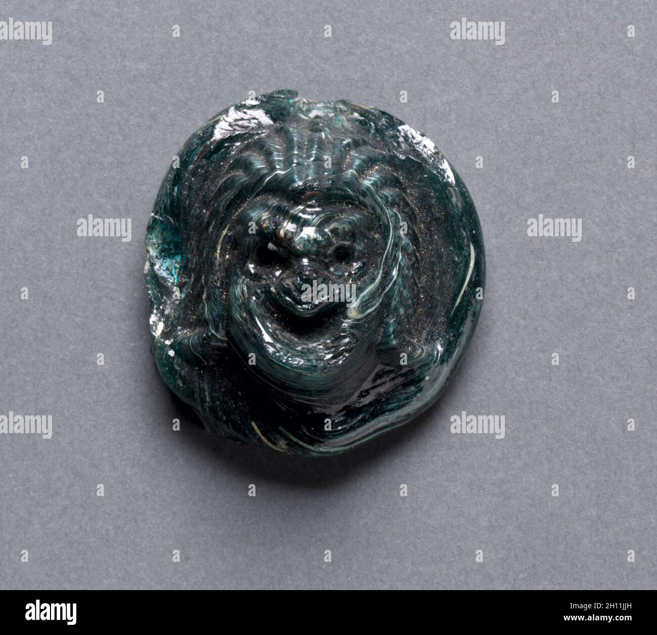 Masque comique, ch. 1er siècle après JC. La Grèce, l'époque gréco-romaine, la fin de la dynastie ptolémaïque à l'Empire romain. Verre vert foncé ; diamètre : 3,6 cm (1 7/16 po) ; total : 1,7 cm (16 in.). Banque D'Images