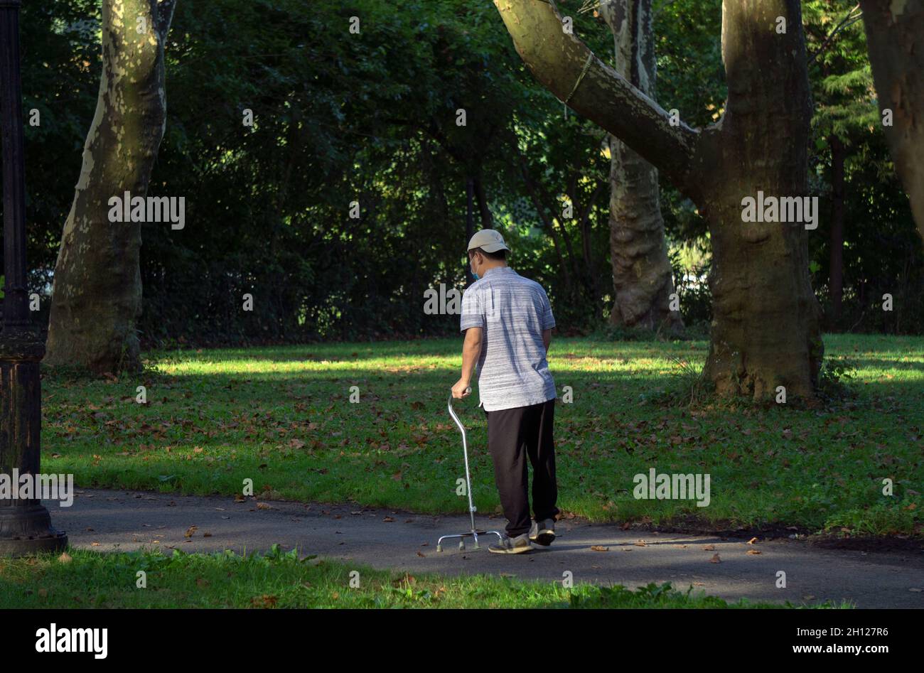Un homme plus âgé marchant avec une canne à quatre pattes sur un sentier pittoresque.Dans un parc à Queens New York, le jour d'automne ensoleillé. Banque D'Images