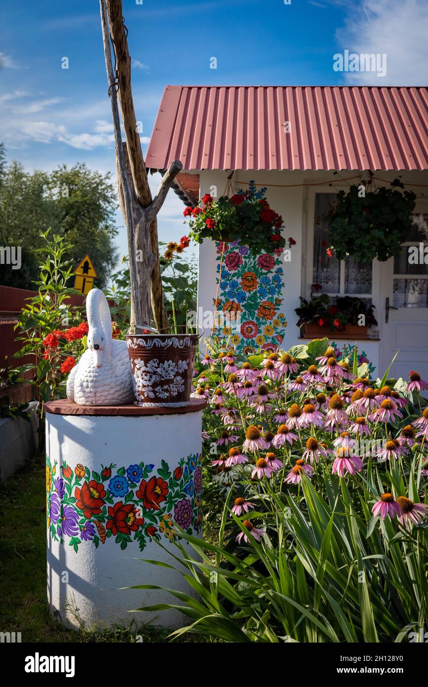 Zalipie, Pologne - 1 août 2021 : un blanc bien peint dans un motif floral coloré, un seau et une statue de cygne sur le dessus.Fleurs roses dans le jardin. Banque D'Images