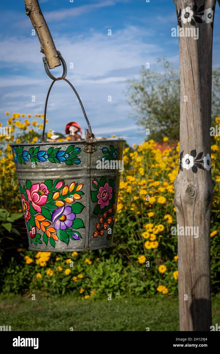 Zalipie, Pologne - 1er août 2021 : puits en bois traditionnel dans le jardin.Un seau peint en motif fleuri coloré.Fleurs jaunes en arrière-plan. Banque D'Images