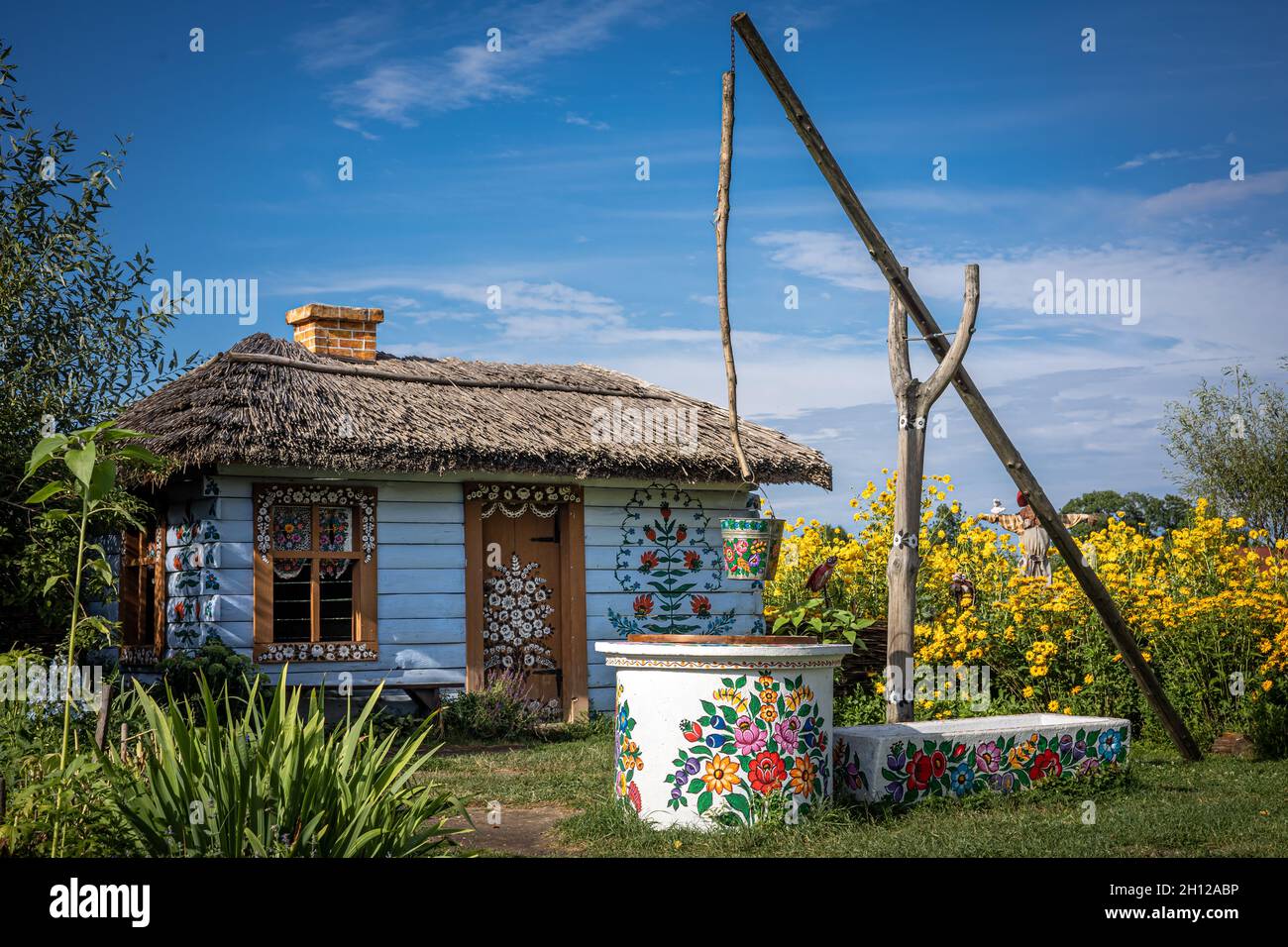 Zalipie, Pologne - 1er août 2021 : un ancien chalet en bois blanc et un puits traditionnel, peint en motifs floraux.Fleurs jaunes dans le jardin. Banque D'Images