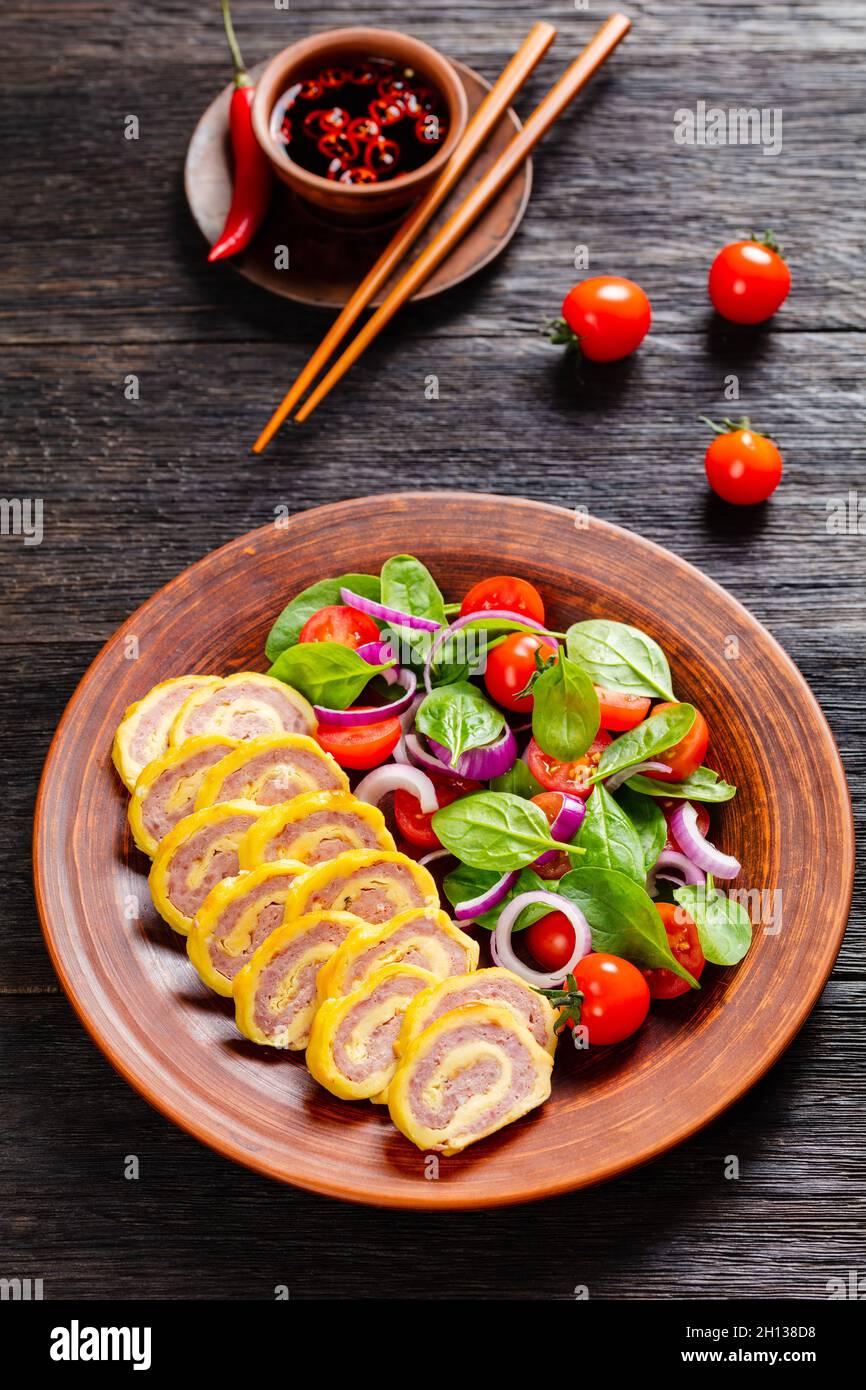petit déjeuner au jambon et au fromage, omelettes, pignons et salade d'oignons rouges aux épinards frais sur une assiette rustique sur une table en bois, vue verticale de Banque D'Images