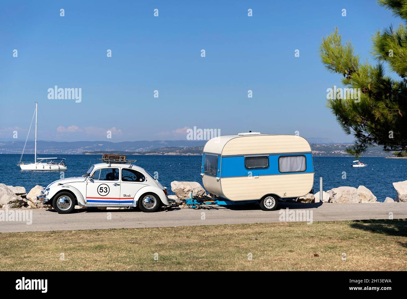 Herbie VW Beetle car avec une remorque d'époque Adria garée au bord de la mer à côté d'un pin Banque D'Images