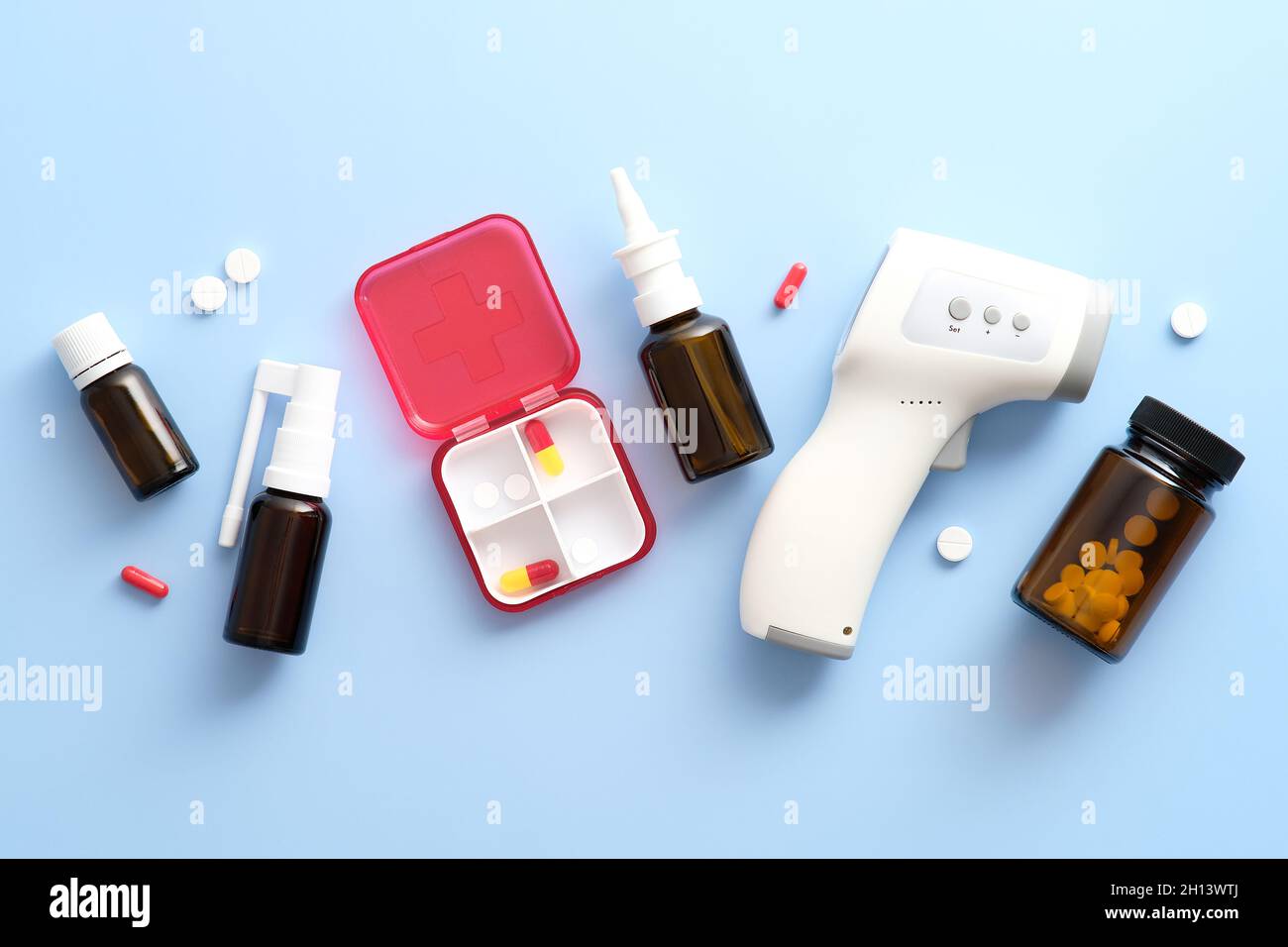 Outils médicaux et médicaments sur fond bleu pastel.Thermomètre numérique plat, kit de premiers soins, spray nasal, pilules. Banque D'Images