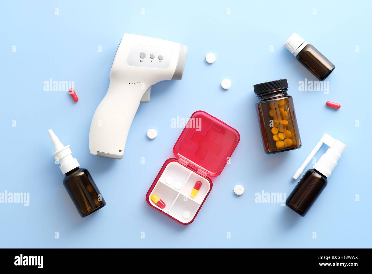 Traitements de la grippe.Vaporisateur nasal, flacon en verre ambré avec pilules, spray contre la toux, thermomètre numérique sur fond bleu pastel.Flat lay, vue de dessus.Médicaments Banque D'Images
