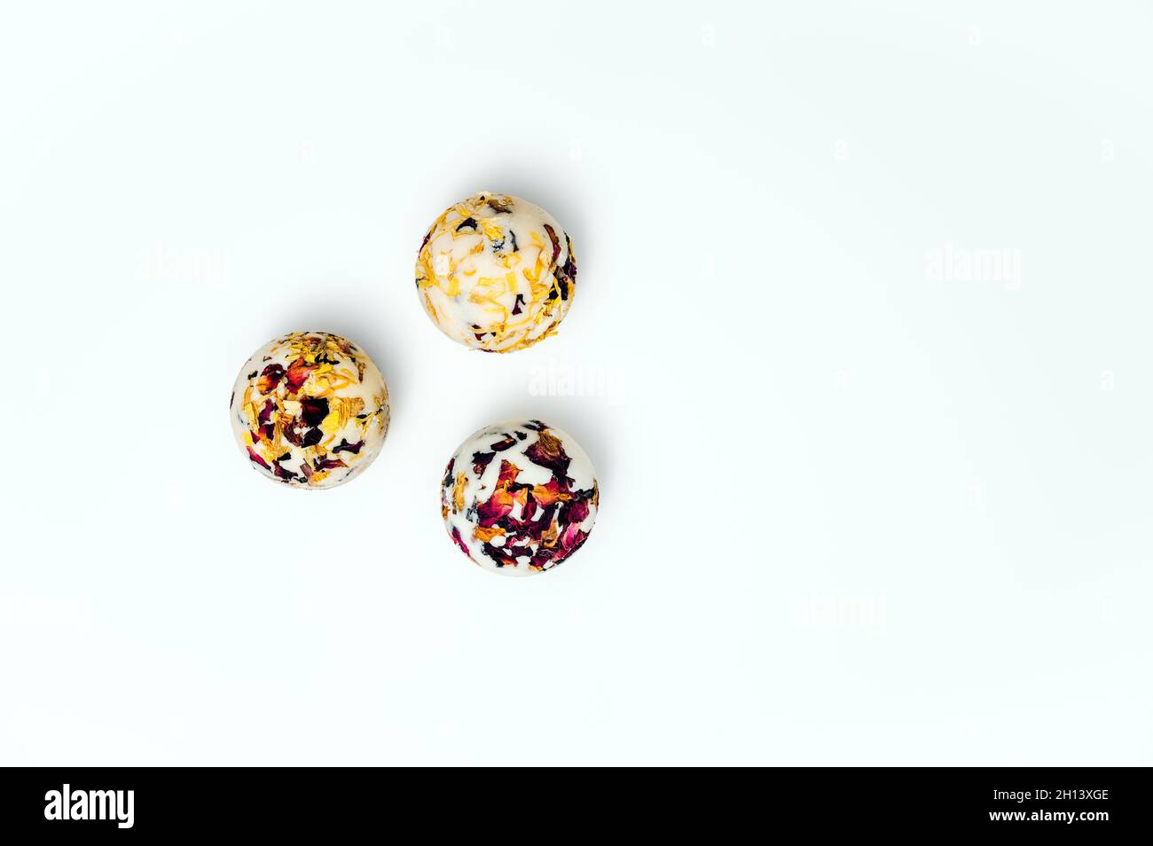 Trois morceaux de savon naturel fait à la main avec des pétales de rose, de malow et de marigold séchés sur fond blanc. Banque D'Images