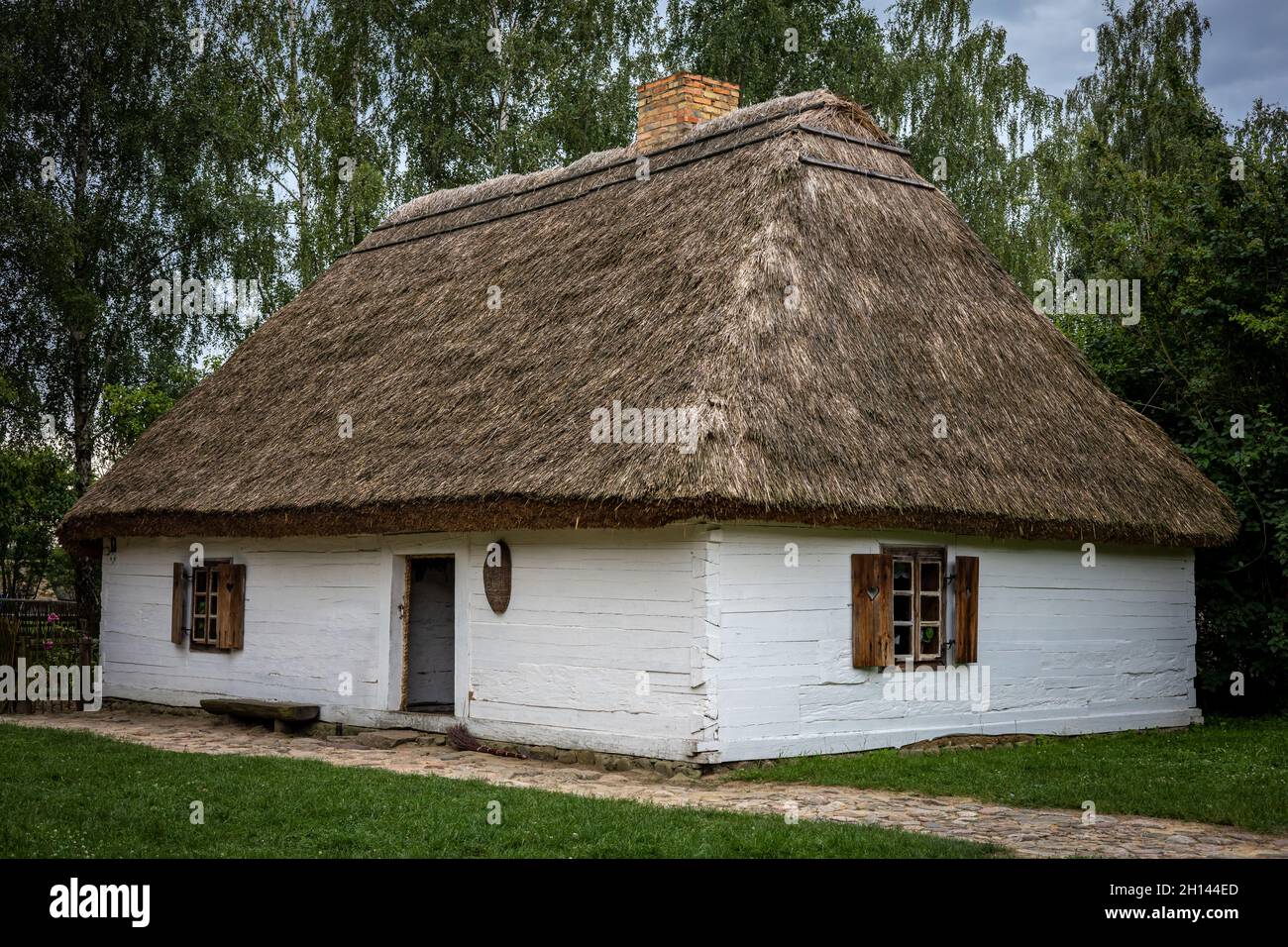 Sierpc, Pologne - 23 juillet 2021 : maison traditionnelle en bois blanc avec toit de chaume, entourée d'arbres.Fenêtres avec volets.Ensoleillé, jour d'été. Banque D'Images