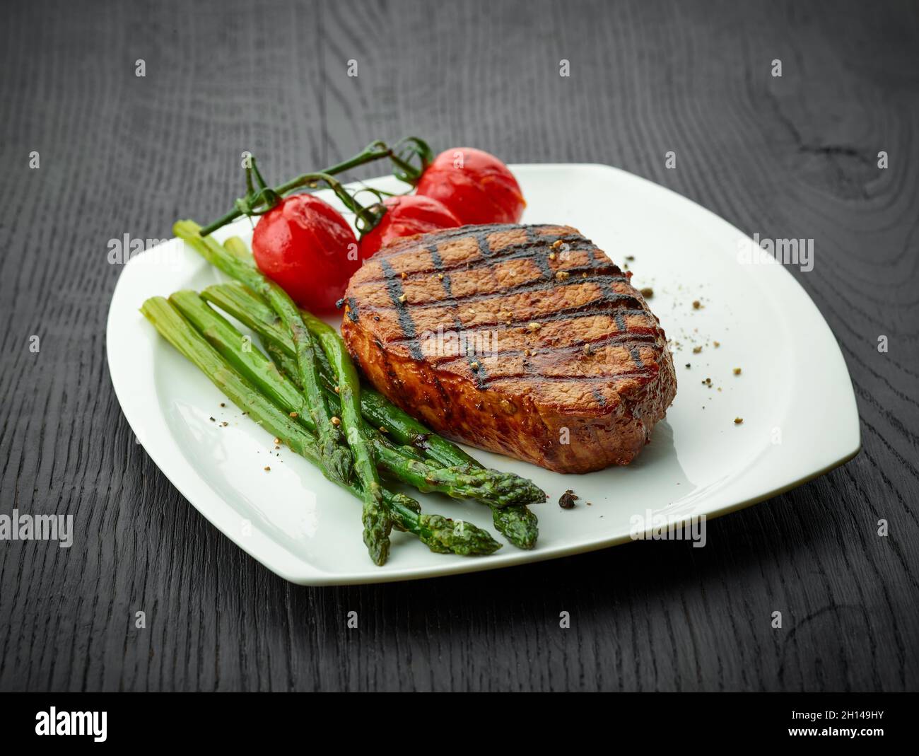 Steak de veau fraîchement cuit, tomates et asperges servis sur une assiette blanche Banque D'Images