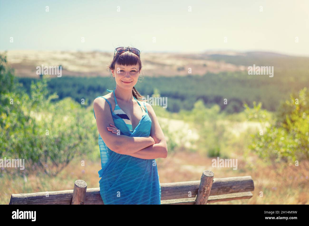 Jeune belle fille en bikini, pareo envelopper et lunettes de soleil sur la tête posant près d'un banc en bois, sourire et regardant l'appareil photo dans dune de Lituanie Curonian Banque D'Images