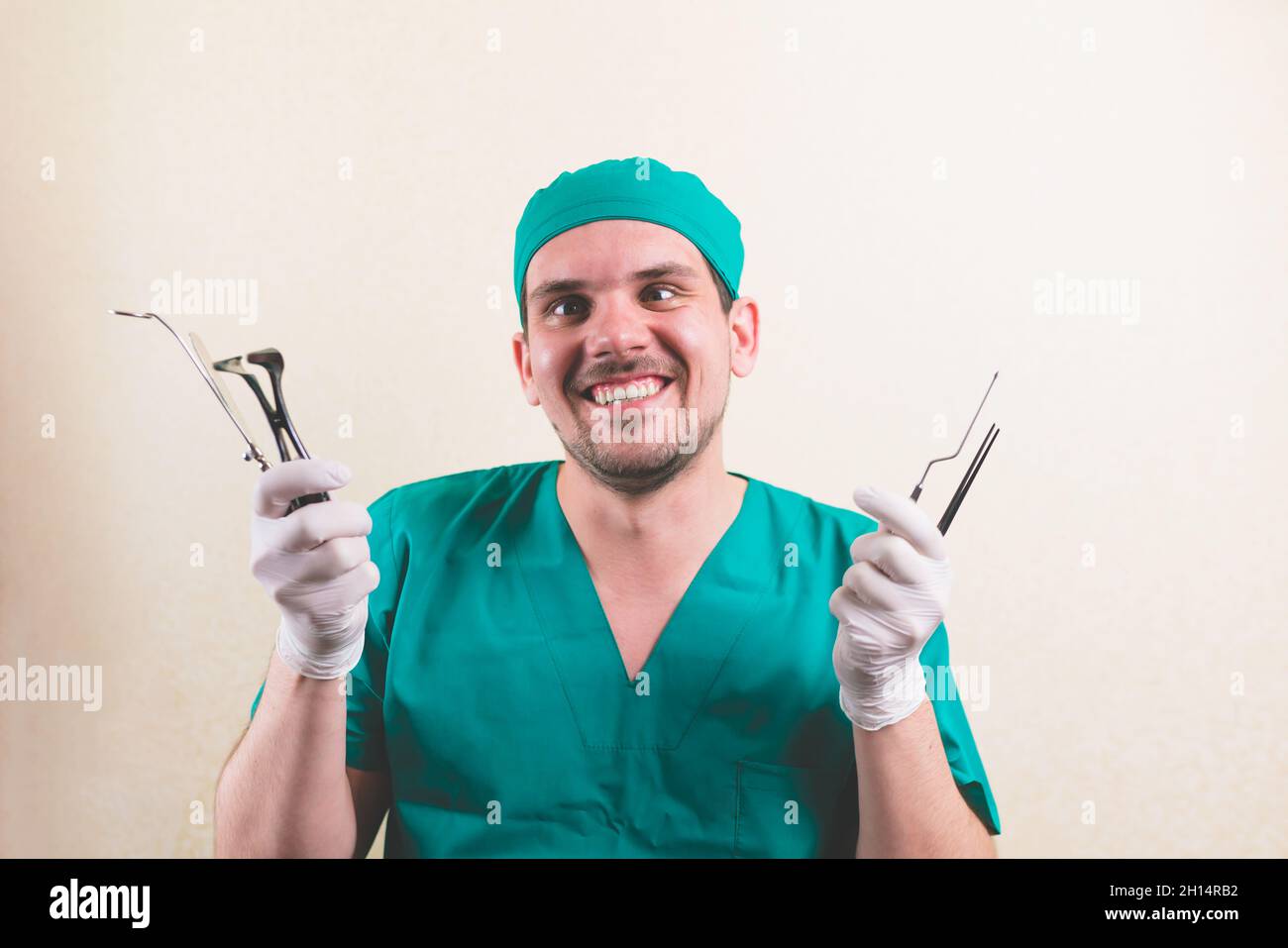 Jeune médecin souriant avec des instruments médicaux dans sa main en costume de chirurgien vert isolé Banque D'Images