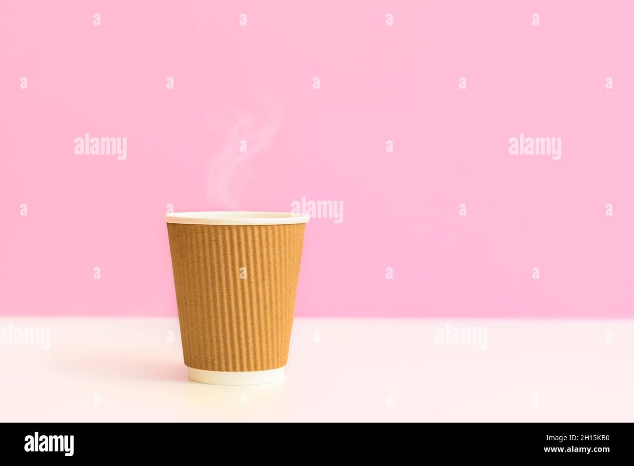 Café chaud avec une tasse en papier jetable sur fond rose clair et blanc avec espace pour les copies.Concept zéro déchet, écologie, remplacement des tasses en plastique Banque D'Images