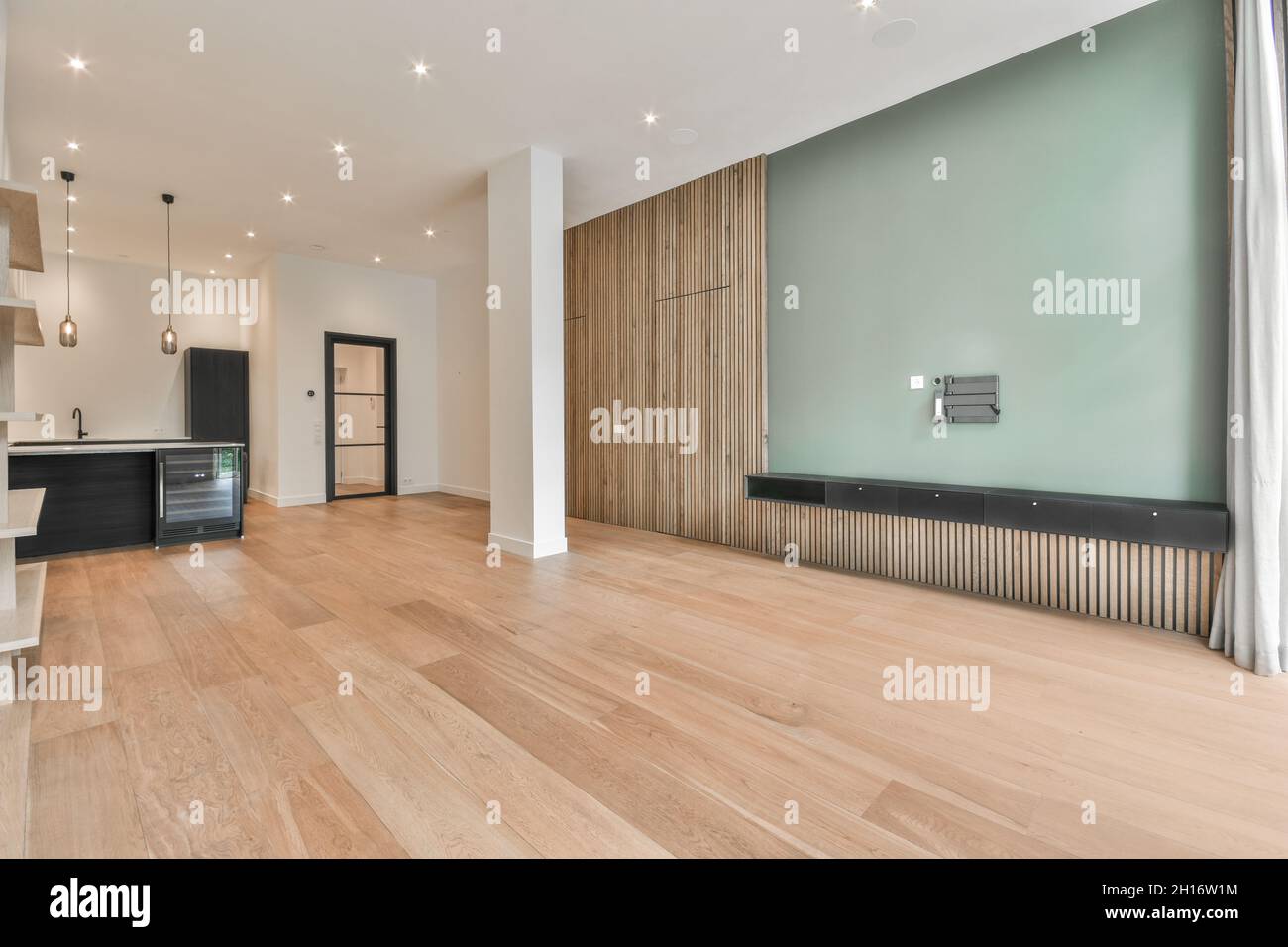 Intérieur d'une cuisine spacieuse avec mobilier noir minimaliste dans un appartement moderne avec murs blancs, parquet et colonnes Banque D'Images