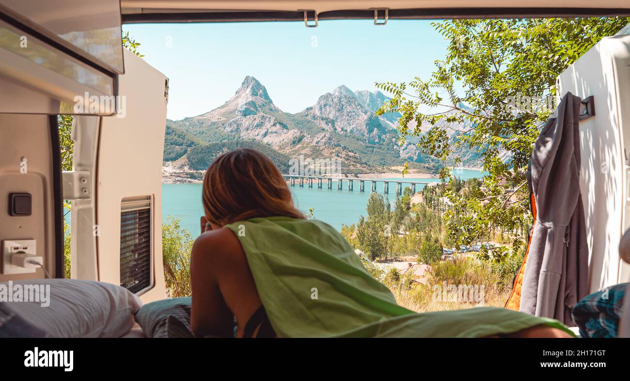 Vue arrière d'une femme voyageur non reconnaissable couché sur un lit en minibus et appréciant le paysage du lac bleu situé dans les montagnes de Riano Banque D'Images