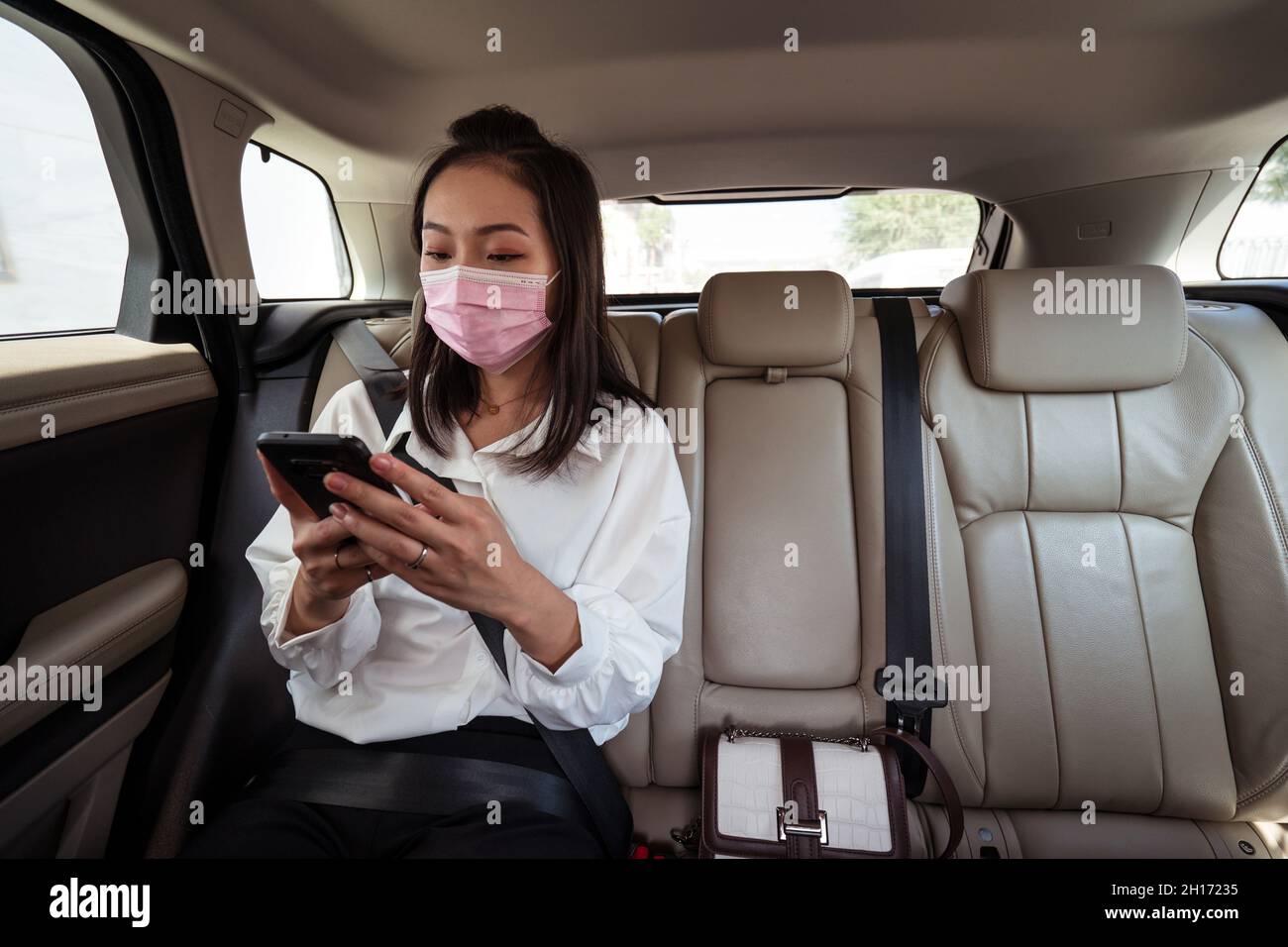 Passager ethnique féminin avec ceinture de sécurité attachée utilisant le  téléphone cellulaire en utilisant le masque de protection sur le siège  arrière en taxi Photo Stock - Alamy