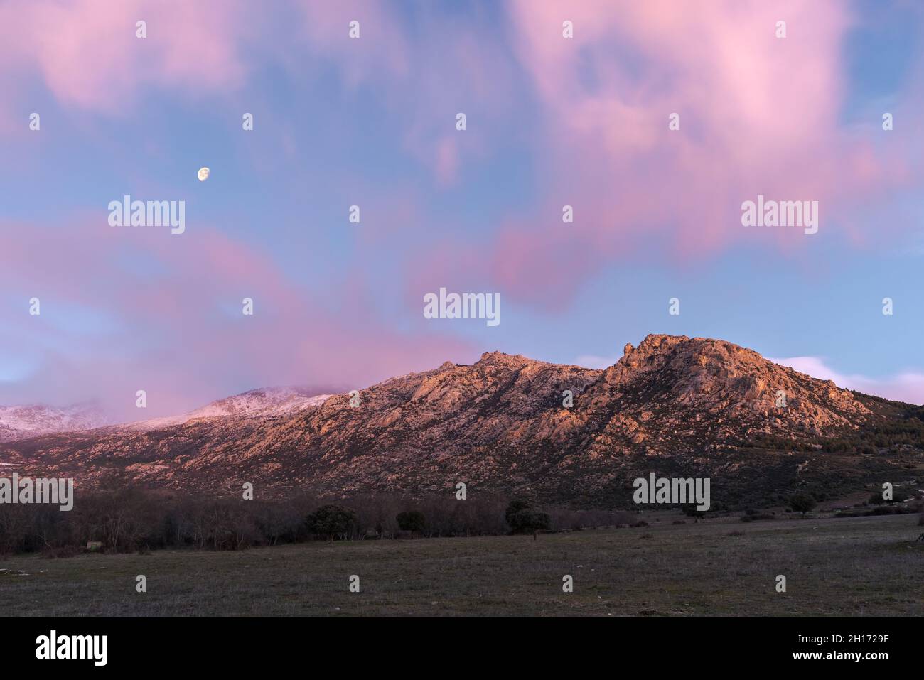 Paysage à couper le souffle de la chaîne de montagnes rocheuses et de la vallée avec des arbres verts sous le ciel de soleil rose avec des nuages et la lune dans la Sierra de Guadarrama National Banque D'Images