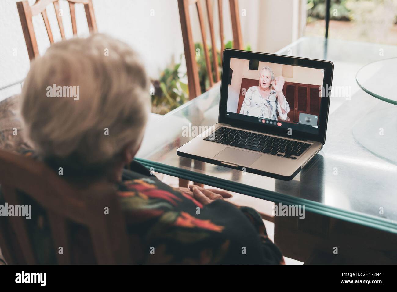 Vue arrière d'une femme âgée méconnue avec de courts cheveux gris assis sur une chaise et écoutant Au revoir de la sœur tout en passant un appel vidéo via le netbook A. Banque D'Images