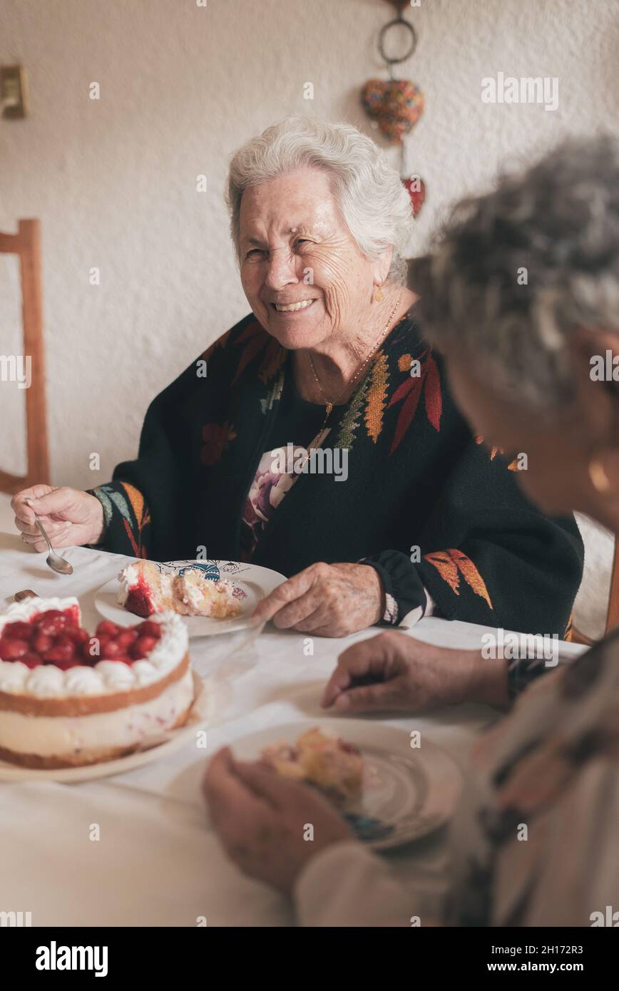 Femme âgée aux cheveux gris et femme sénior assis à la table à manger et célébrant l'anniversaire de 90th avec un délicieux gâteau aux bougies Banque D'Images