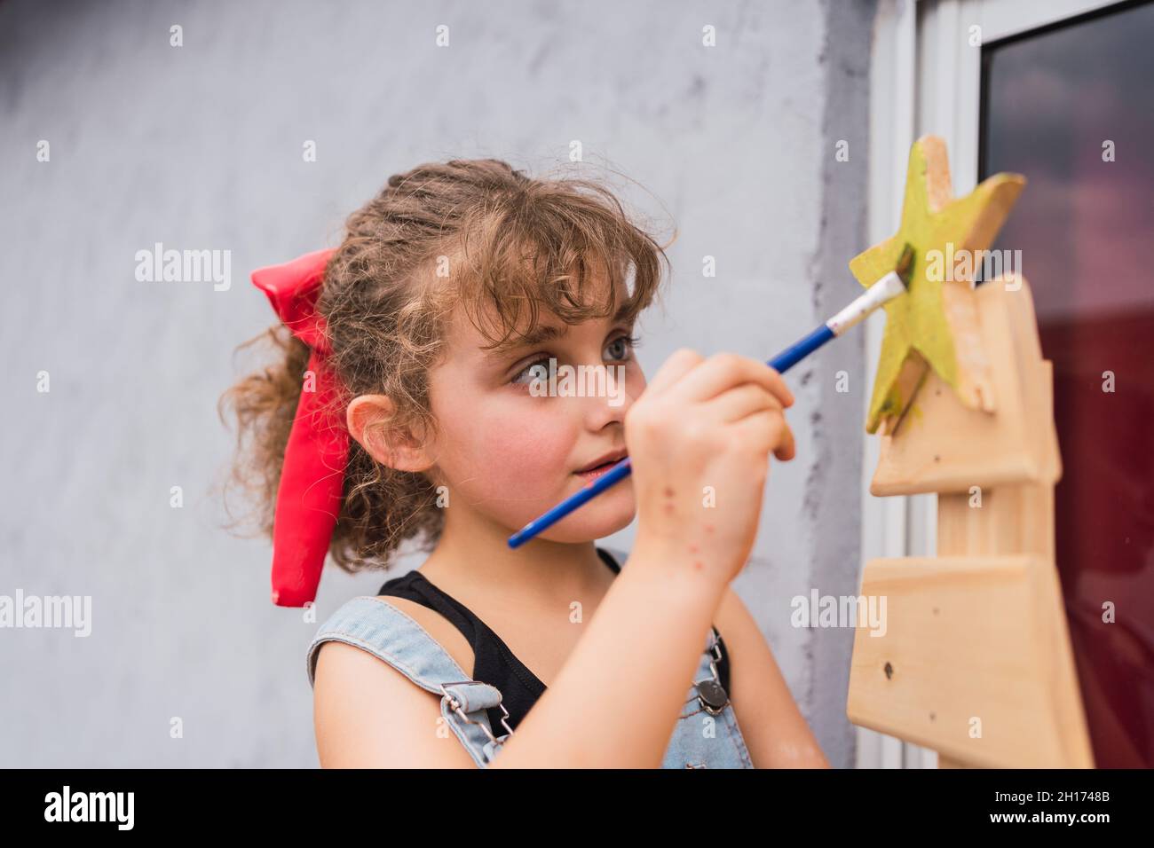Mise au point fille en denim peinture générale avec pinceau sur arbre de Noël décoré dans la pièce lumineuse pendant la préparation des vacances à la maison Banque D'Images