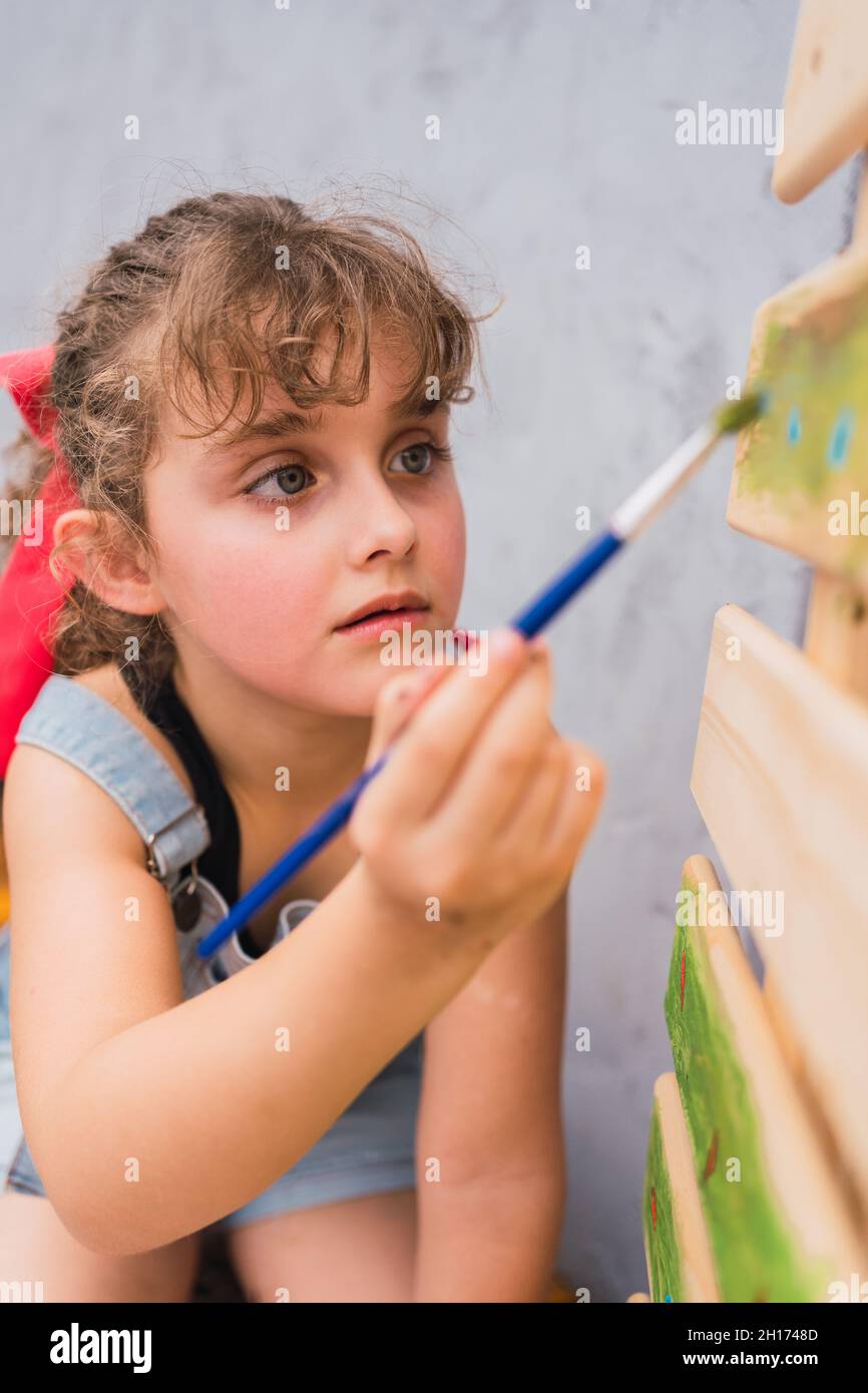 Mise au point fille en denim peinture générale avec pinceau sur arbre de Noël décoré dans la pièce lumineuse pendant la préparation des vacances à la maison Banque D'Images