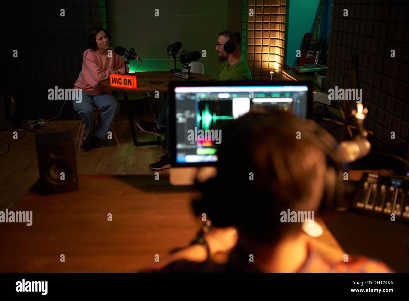 Vue arrière d'un directeur du son masculin méconnaissable assis à une table avec un ordinateur pendant l'enregistrement de podcast avec l'hôte et la chanteuse féminine dans un studio sombre Banque D'Images