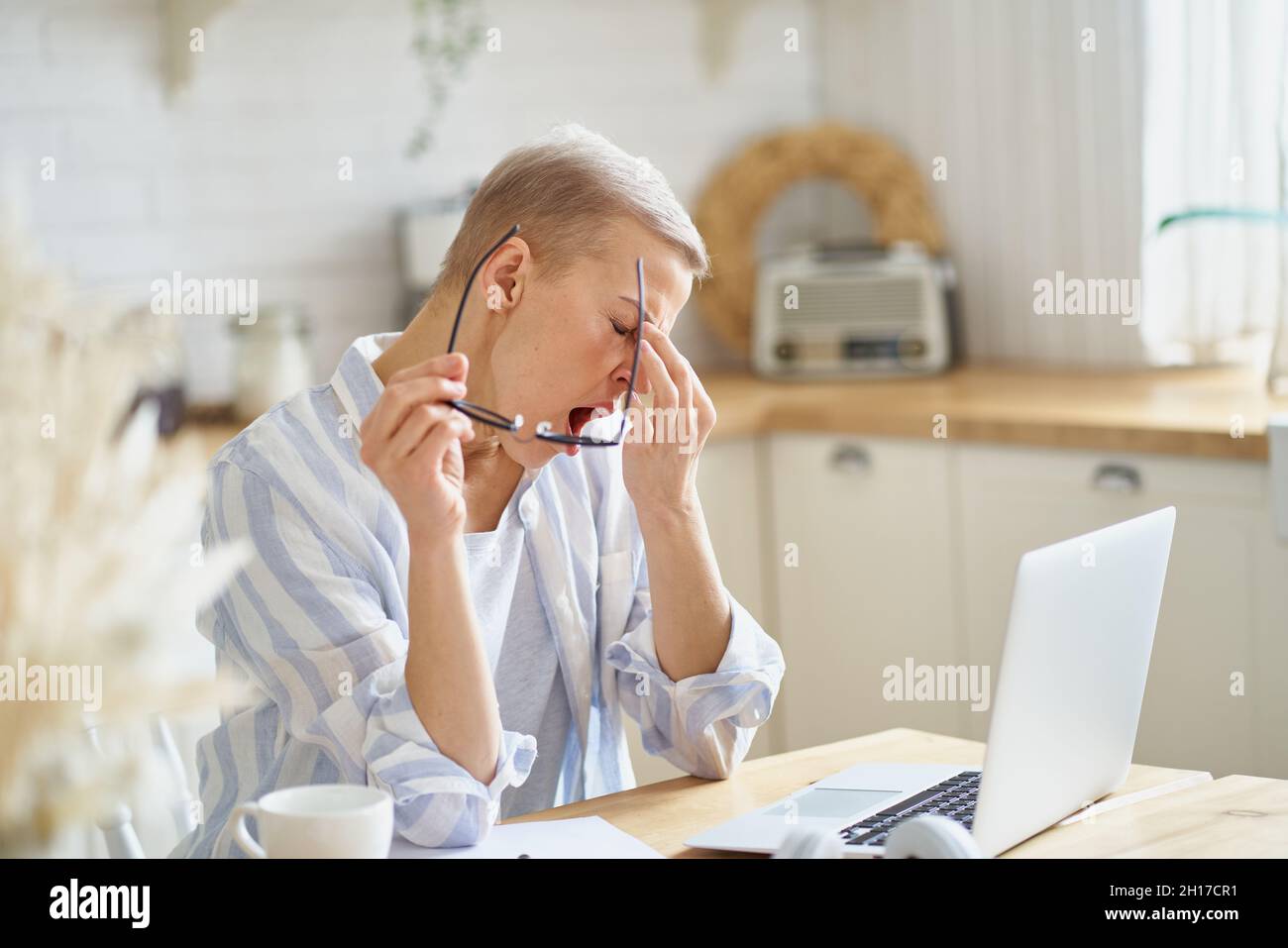 Femme d'âge moyen massant le nez et se sentant endormi tout en travaillant sur un ordinateur portable en ligne depuis chez elle Banque D'Images