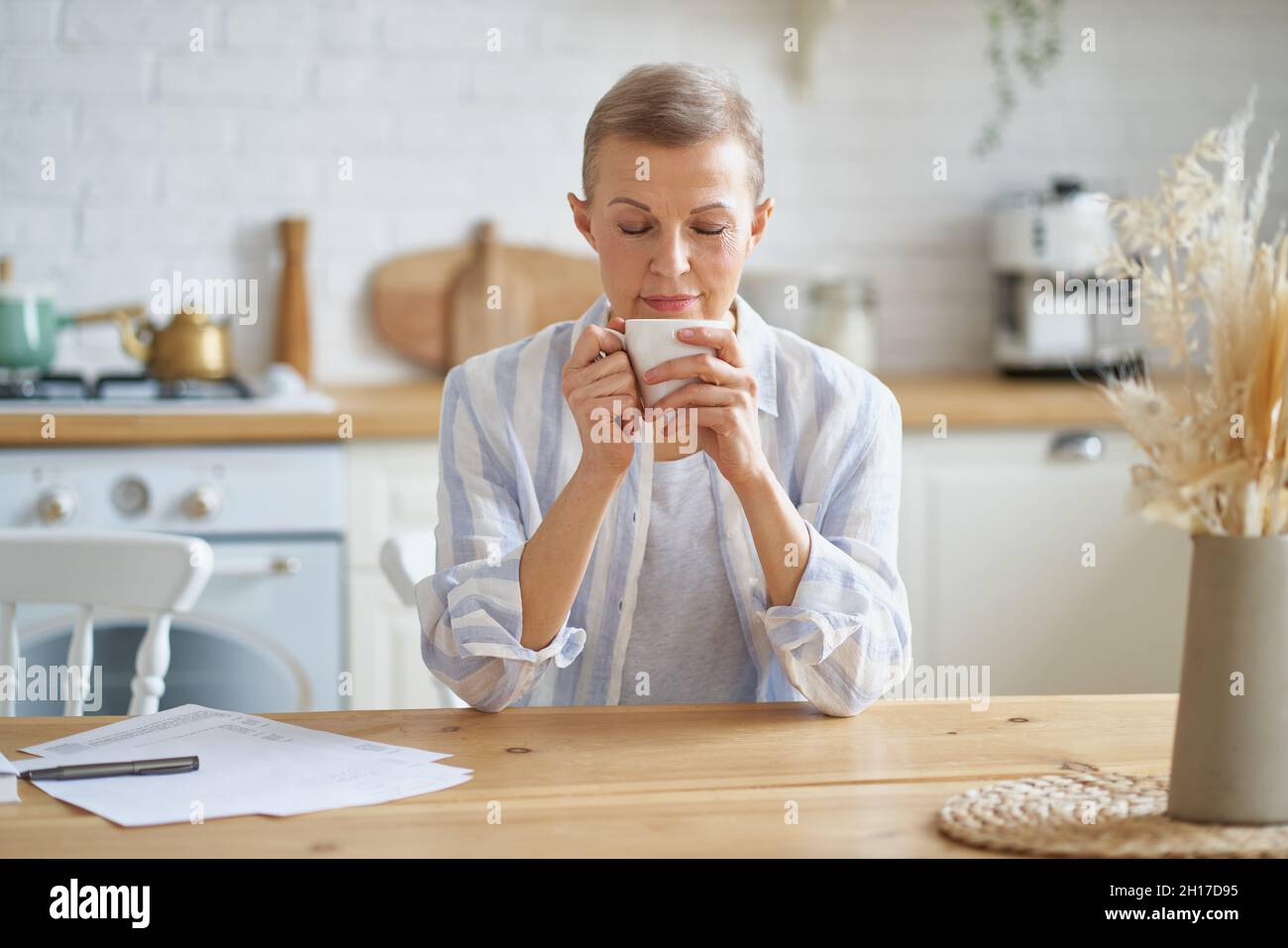 Belle femme mûre commençant le jour avec le café tout en étant assis à une table en bois dans la cuisine Banque D'Images