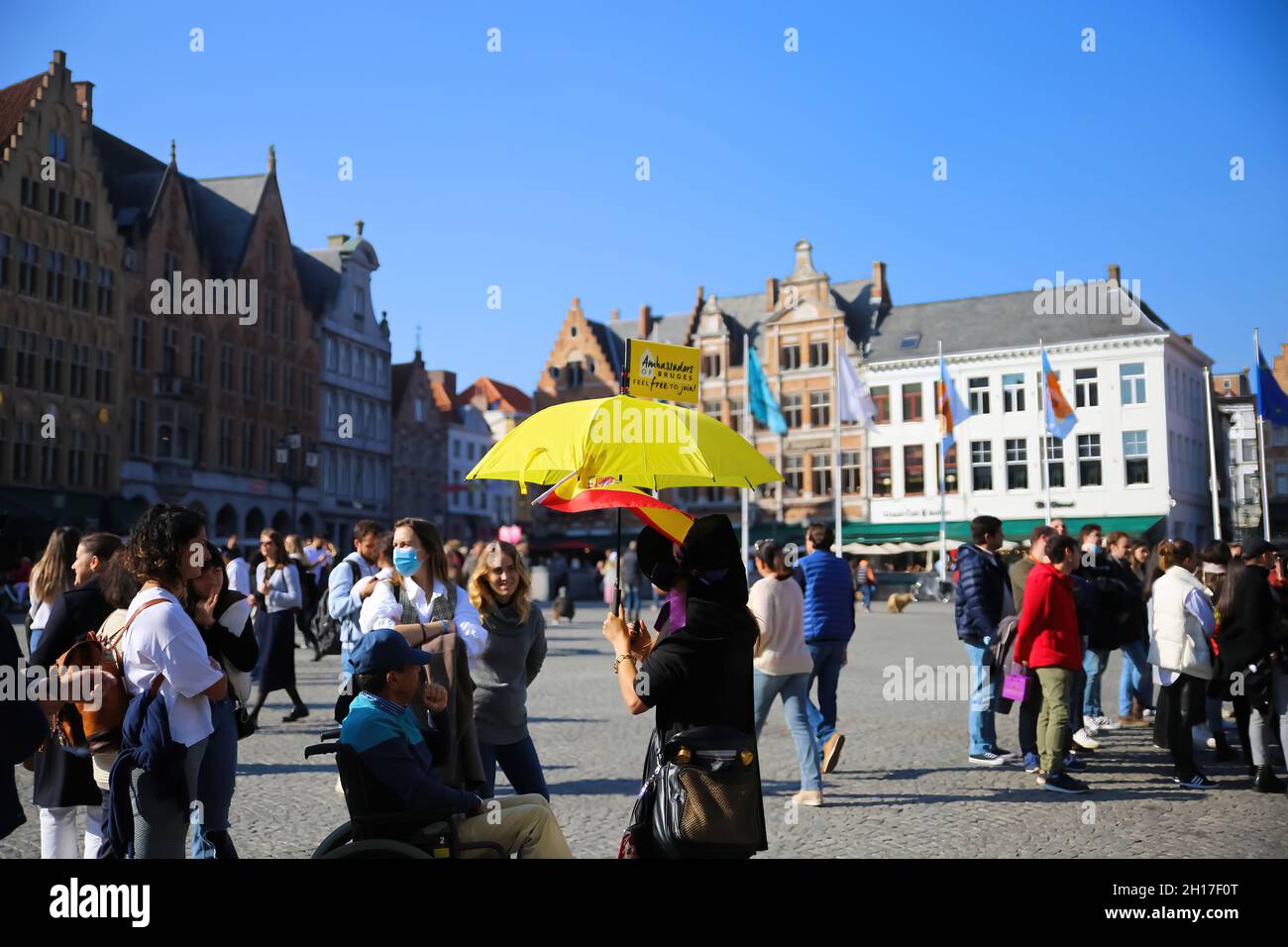 Brugge (groote markt), Belgique - octobre 9.2021: Vue sur le groupe touristique et guide touristique avec parapluie jaune sur la place du marché contre ciel bleu clair Banque D'Images