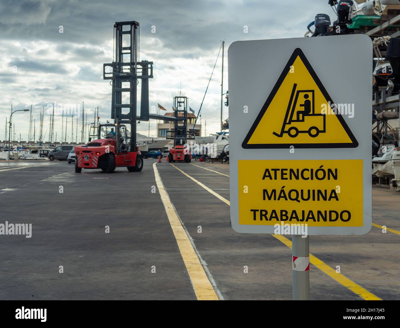 Gros plan d'une affiche de, danger machine working écrit en espagnol.En arrière-plan, hors foyer, un bateau transportant une machine plaçant des bateaux sur un moi Banque D'Images