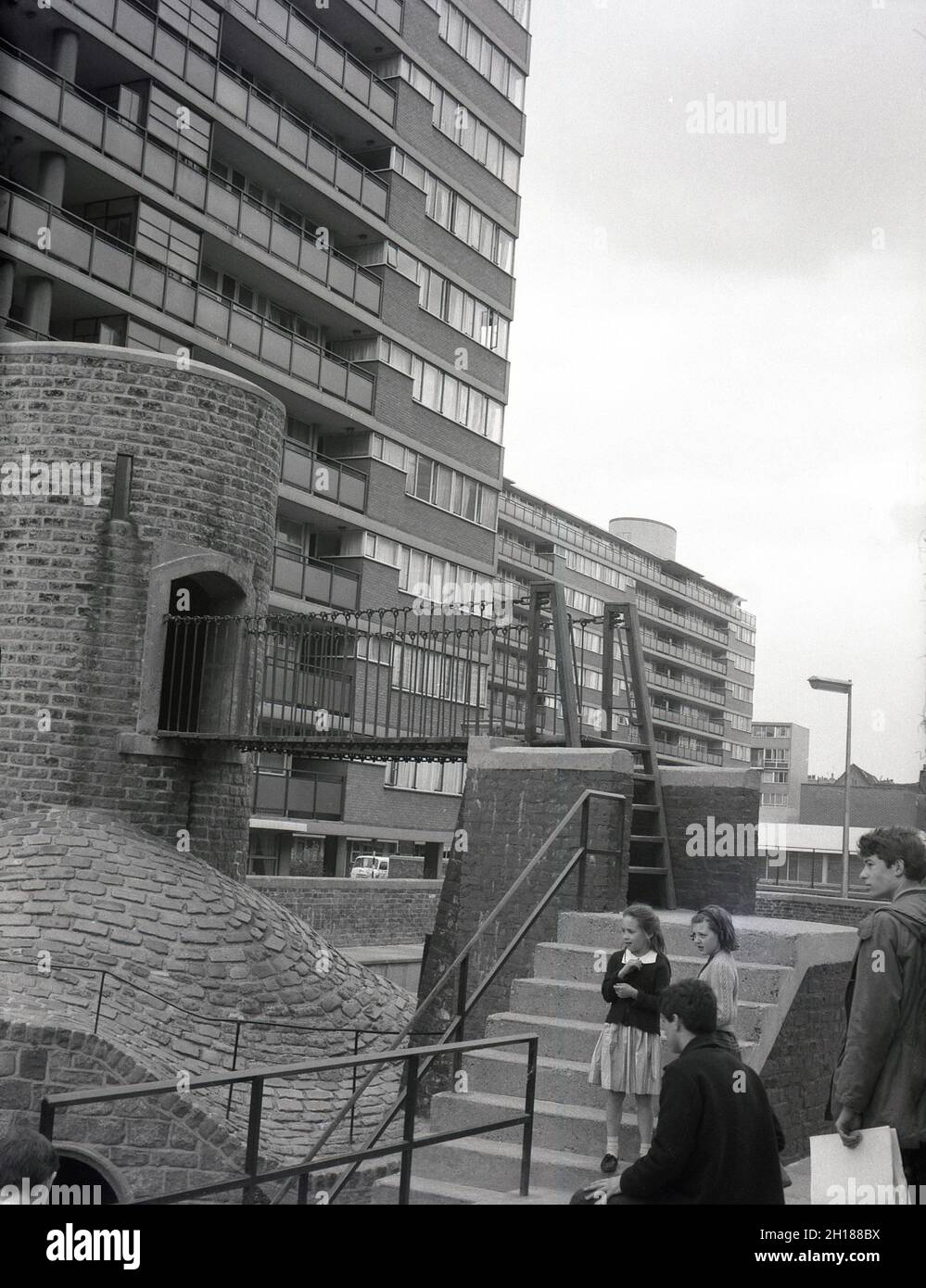 Années 1960, historique, enfants à l'extérieur à côté d'une aire de jeux en béton et en briques, dans un grand domaine de logement de conseil, Churchill Gardens à Pimlico, dans le centre de Londres, Angleterre, Royaume-Uni.Construit entre 1948 et 1962 pour remplacer les terrasses victoriennes endommagées dans le Blitz de la Seconde Guerre mondiale, c'était un immense domaine de logements sociaux modernes, avec 32 blocs de tour fournissant 1,600 maisons. Banque D'Images