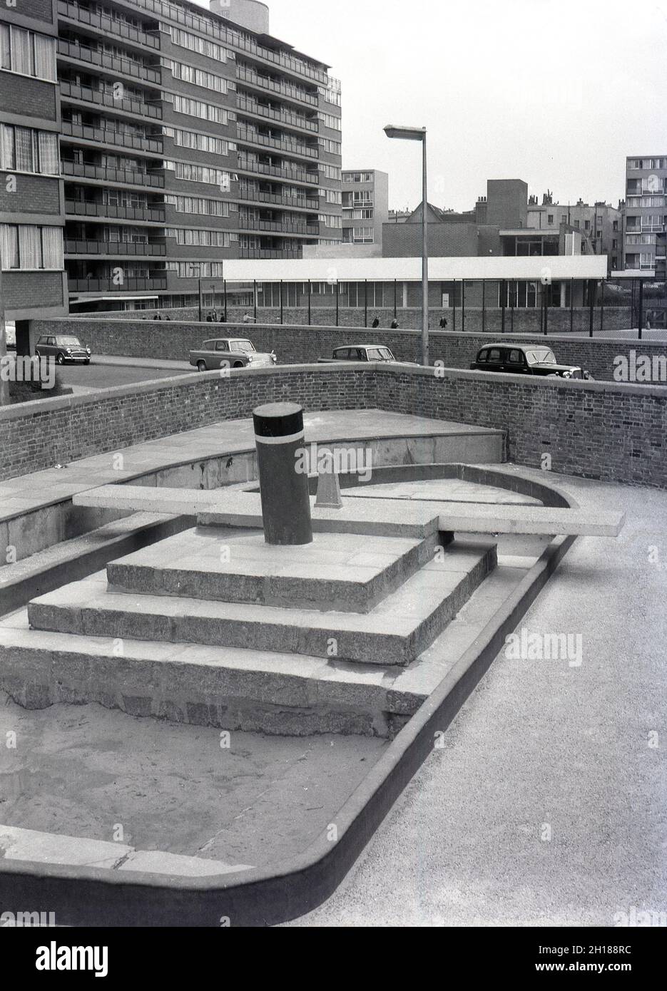 Années 1960, historique, terrain de jeu en béton et clos à l'extérieur d'un grand domaine de logement de conseil, Churchill Gardens à Pimlico, dans le centre de Londres, Angleterre, Royaume-Uni.Construit entre 1948 et 1962 pour remplacer les terrasses victoriennes endommagées dans le Blitz de la Seconde Guerre mondiale, c'était un immense domaine de logement social, avec 32 blocs de tour fournissant 1,600 maisons.À l'extérieur des appartements, une enceinte fortifiée avec une aire de jeux en béton et un bac à sable en forme de bateau. Banque D'Images