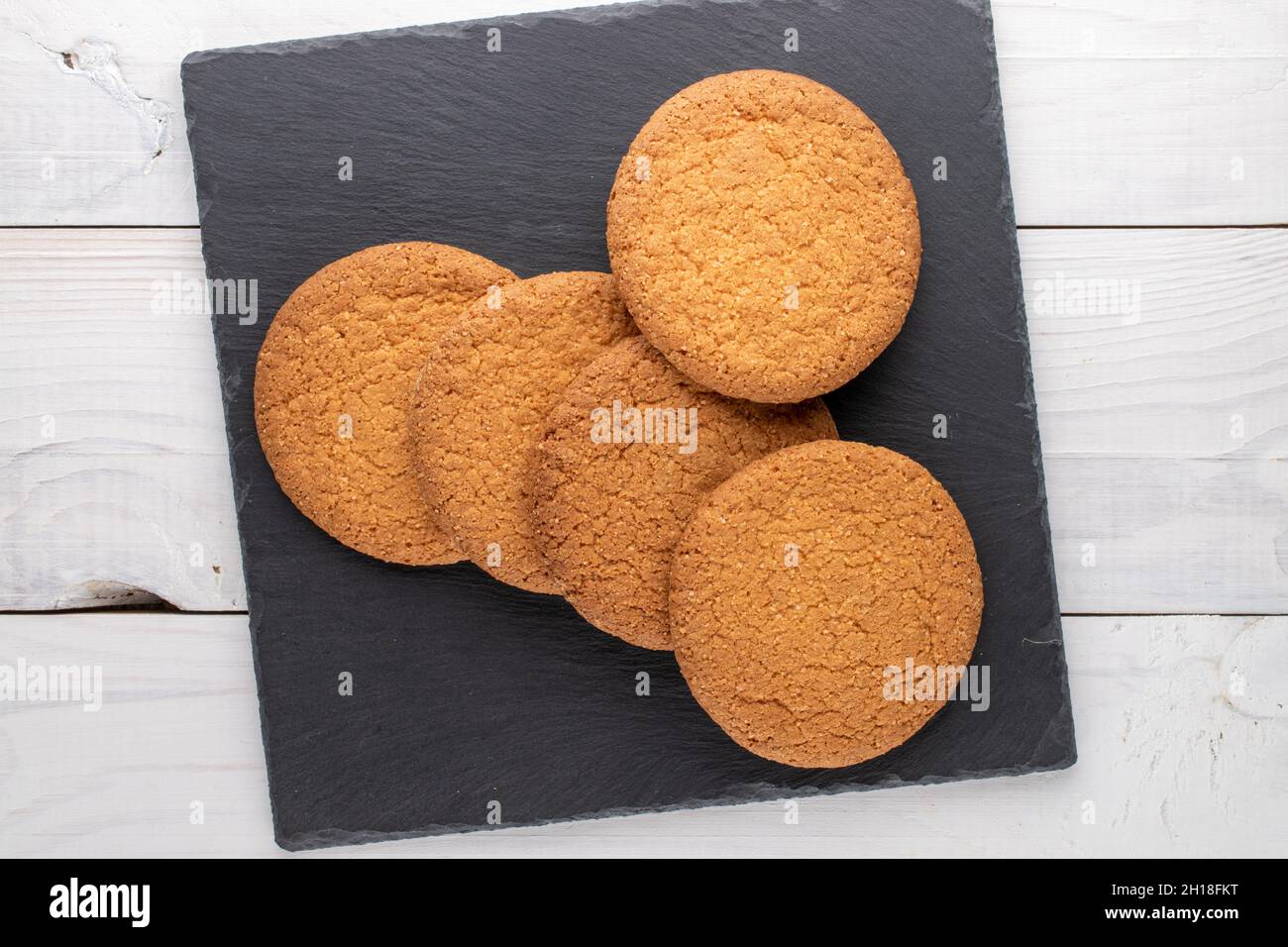 Plusieurs délicieux biscuits américains ronds sur un tableau d'ardoise, gros plan, sur une table en bois, vue du dessus. Banque D'Images