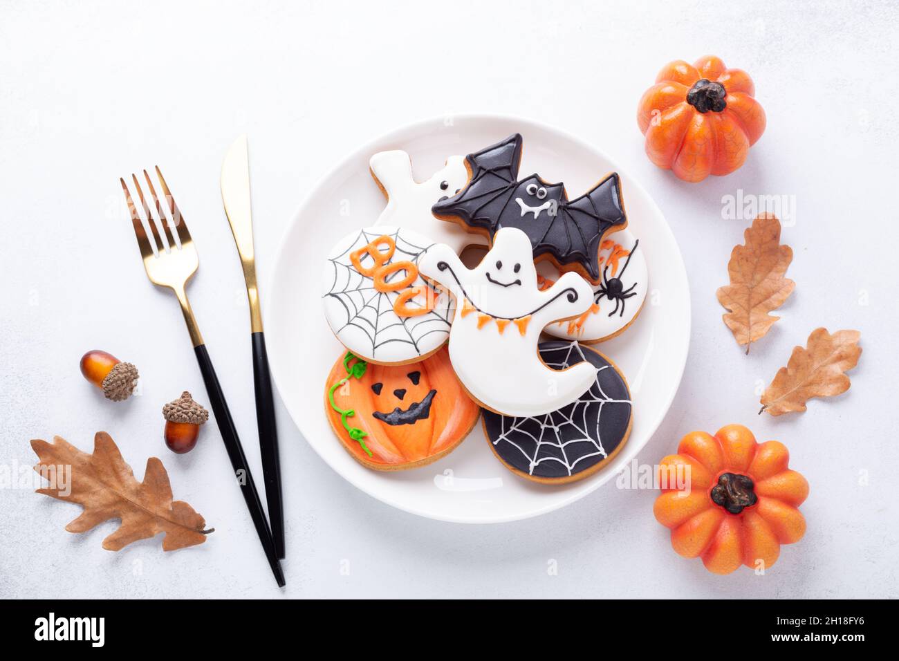 Table d'Halloween avec biscuits au pain d'épice sur plaque blanche et amèrement sur fond blanc.Biscuits maison lumineux pour Halloween partie - image Banque D'Images