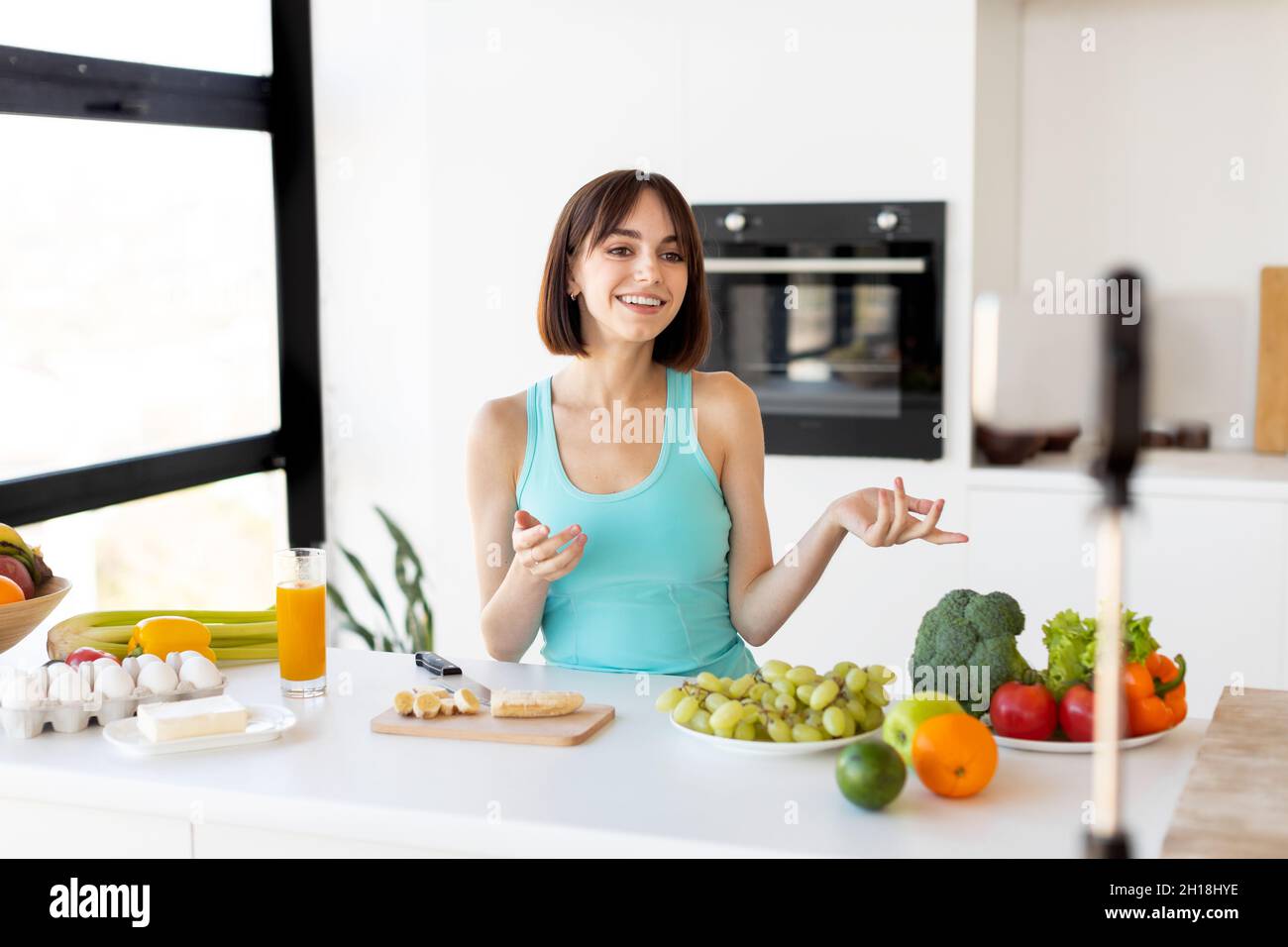 Concept de blogueur de nourriture.Femme millénaire enregistrant une nouvelle recette vidéo sur smartphone, debout dans un intérieur de cuisine moderne Banque D'Images