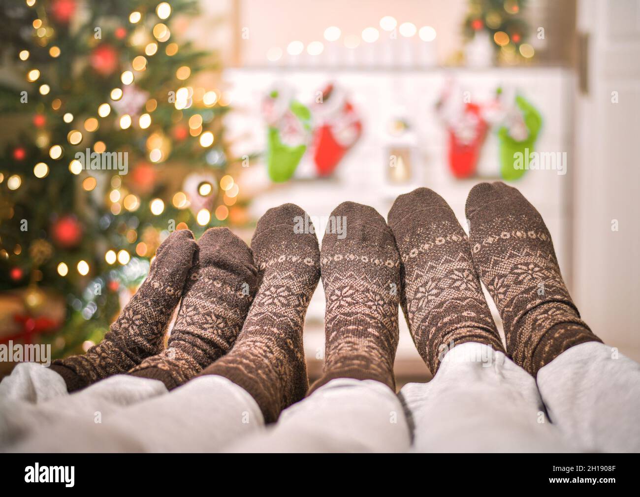 Trois paires de chaussettes en laine de différents âges pour les jambes.À Noël, en face d'un sapin de Noël étincelant décoré et de chaussettes cadeau suspendues sur une commode. Banque D'Images