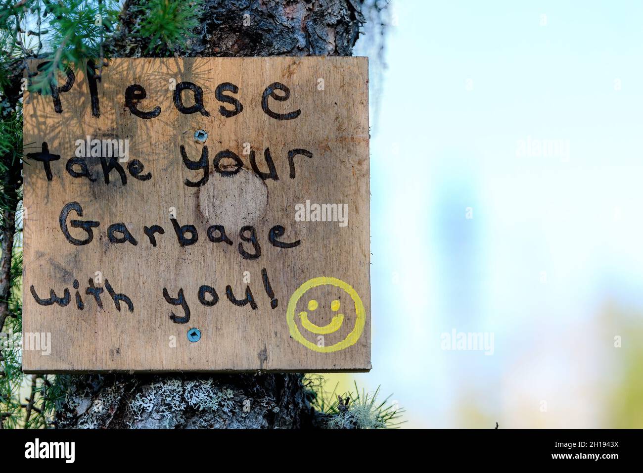 Un panneau peint à la main dans les bois demandant aux gens de prendre leurs ordures quand ils partent.Le signe est attaché à une arborescence.Visage souriant dessiné sur l'affiche. Banque D'Images