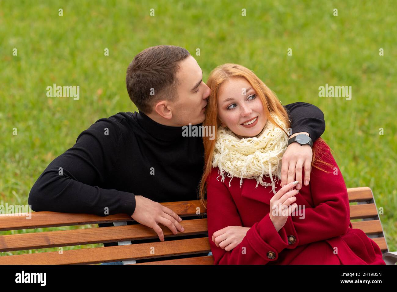 jeune couple romantique sur un banc de parc, le gars chuchote dans l'oreille de la fille Banque D'Images
