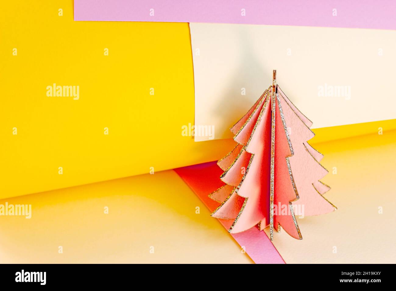 Arbre de Noël rose en bois brillant sur papier jaune et magenta coloré tourbillonne de papier abstrait avec espace de copie.Simple nouvel an et vacances de Noël t Banque D'Images