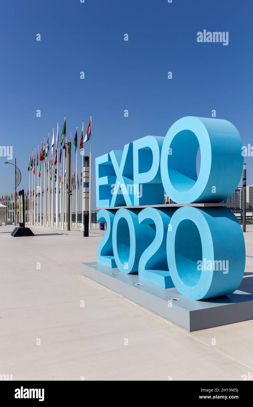 Dubaï, Émirats arabes Unis, 17.10.2021.Affiche du logo bleu de l'Expo 2020 à l'entrée du quartier de la mobilité du site de l'Expo avec drapeaux nationaux des participants en arrière-plan. Banque D'Images