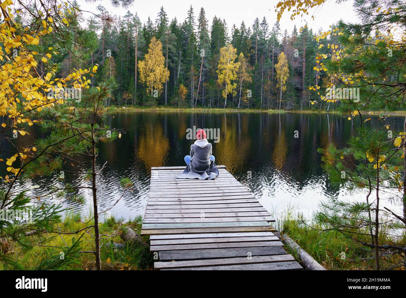 Une jeune femme s'assoit sur le quai en admirant le paysage de la forêt d'automne, lac avec des arbres dorés jaunes colorés Banque D'Images