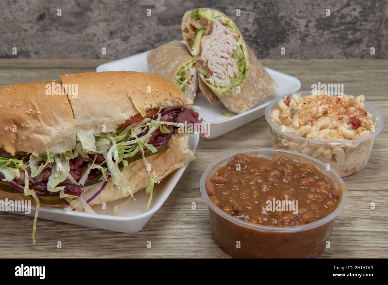 Des sandwichs déli faits à la main à base d'ingrédients frais avec du rôti de bœuf sur un rouleau italien devant du filet de dinde, des haricots cuits et de la salade de macaroni. Banque D'Images