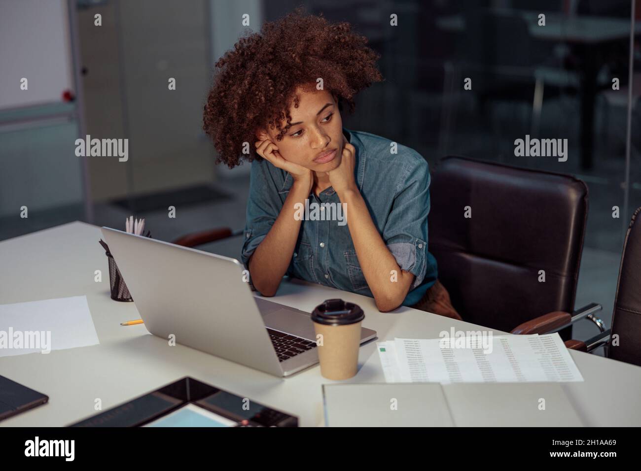 Femme afro-américaine fatiguée utilisant un ordinateur portable et des documents Banque D'Images