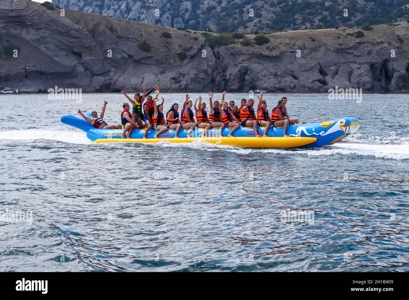 Une foule de personnes dans des gilets de sauvetage dans la mer sur une banane gonflable contre une côte rocheuse.Des gens heureux dans une station balnéaire.République de Crimée, Suda Banque D'Images