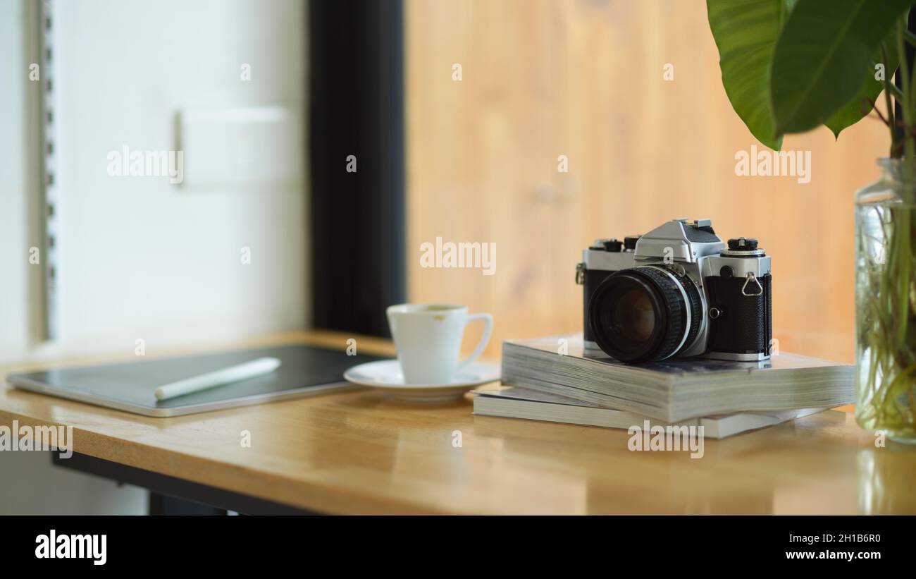 Gros plan espace de travail portable dans un café avec appareil photo d'époque sur un livre, une tasse à café et une tablette numérique sur une table en bois. Banque D'Images