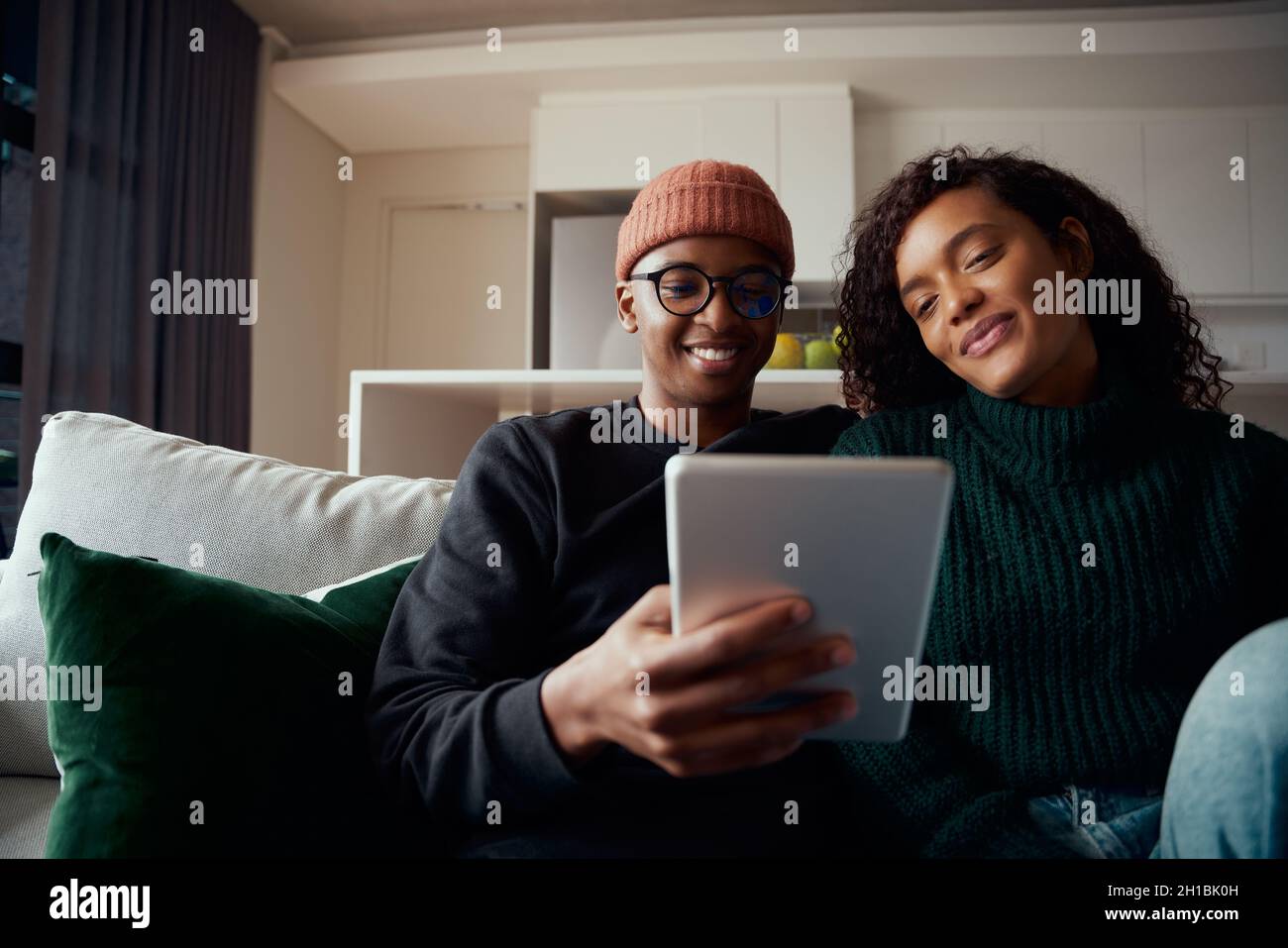 Jeune couple adulte, multiethnique, assis sur un canapé dans un appartement moderne avec une tablette Banque D'Images