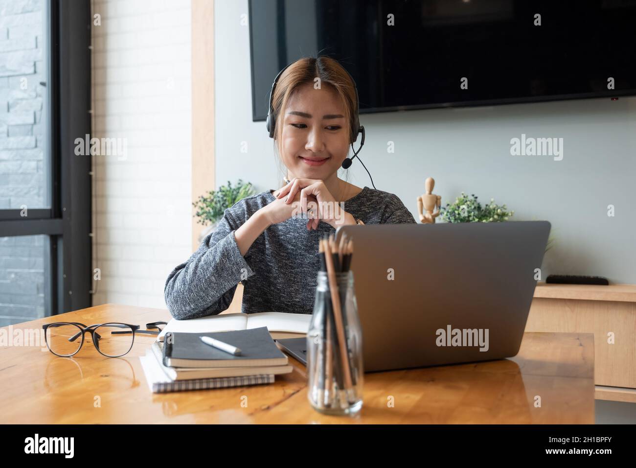 Prise de vue rognée femme asiatique souriante freelancer portant un casque, communiquant avec le client via un appel vidéo sur ordinateur.Professionnel agréable millénaire Banque D'Images